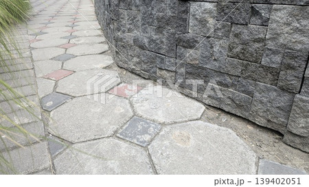 High angle view shows curved dark stone wall beside hexagonal pavement tiles. Grey masonry, red accents create geometric patterns. This durable surface suits architecture, landscaping, urban design. 139402051