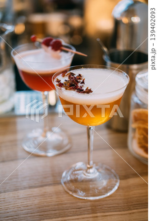 Garnished cocktail. Refreshing liquor mix. Stemmed glass with frothy liquid on tray. Restaurant alcohol with dried petals on wooden table. 139402093