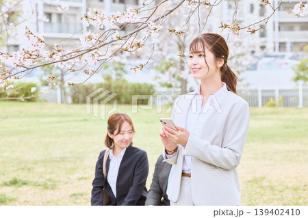 桜の下でスマートフォンを持つ白スーツの若い女性ビジネスパーソンと同僚・春の新生活イメージ 桜の下でスマートフォンを持つ白スーツの若い女性ビジネスパーソンと同僚・春の新生活イメージ 139402410