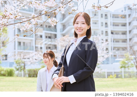 桜の咲くキャンパスでスーツ姿の若い女性・就職活動中の女子大学生が笑顔で立つ春の入社式イメージ 139402416