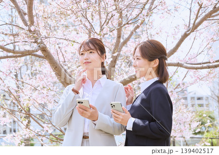 桜の下でスマートフォンを持ちながら会話する二人の若い女性ビジネスパーソン・新入社員の春のイメージ 桜の下でスマートフォンを持ちながら会話する二人の若い女性ビジネスパーソン・新入社員の春のイメージ 139402517