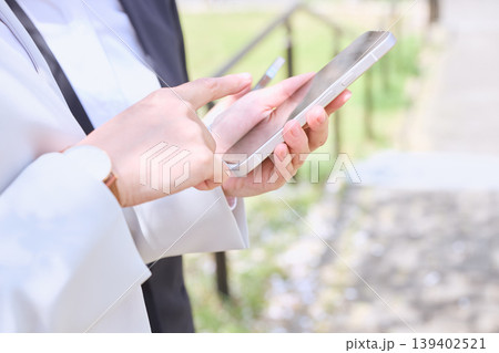 屋外でスマートフォンを操作する白いジャケットの女性ビジネスパーソン・モバイルワークのイメージ 139402521