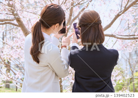 春の桜の下でスマートフォンで写真を撮る二人のビジネスウーマン・お花見を楽しむスーツ姿の女性会社員 春の桜の下でスマートフォンで写真を撮る二人のビジネスウーマン・お花見を楽しむスーツ姿の女性会社員 139402523