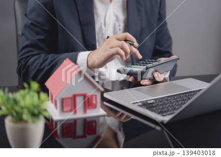 Businessman using calculator for calculating finance on table with house model. Real estate, tax, and property investment concept. 139403018