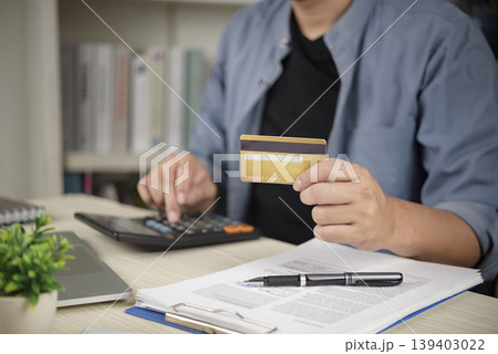 Man holding credit card and using calculator for financial planning, paying bills, checking debt balance, and online shopping at home office desk. 139403022