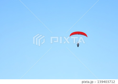 Red parachute soars against vast, clear blue sky Red parachute soars against vast, clear blue sky 139403712