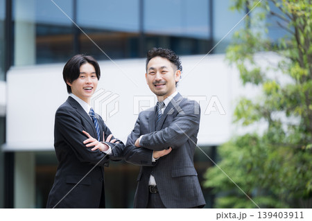 ビルの前で信頼感あるスーツの営業法人営業と企業成長イメージ カメラ目線の笑顔上司と部下の腕組み ビルの前で信頼感あるスーツの営業法人営業と企業成長イメージ カメラ目線の笑顔上司と部下の腕組み 139403911