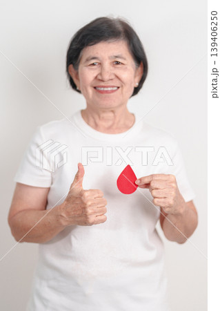 Elderly woman with red Blood drop paper for concept of June World Blood Donor day, Donation, April Hemophilia awareness day, May Thalassemia Day, Anemia awareness, June Sickle Cell and Blood Disorders Elderly woman with red Blood drop paper for concept of June World Blood Donor day, Donation, April Hemophilia awareness day, May Thalassemia Day, Anemia awareness, June Sickle Cell and Blood Disorders 139406250