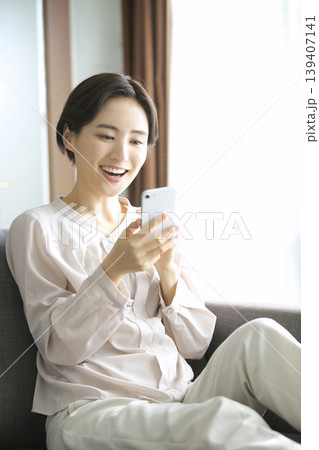 スマートフォンを見て笑顔になる女性 自宅でくつろぐ日常のひととき スマートフォンを見て笑顔になる女性 自宅でくつろぐ日常のひととき 139407141
