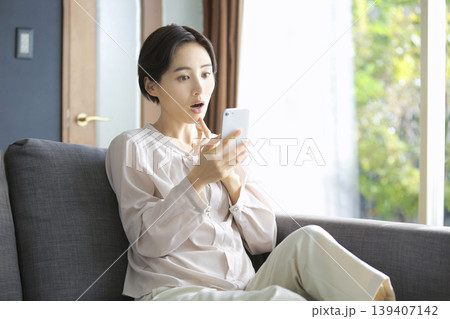 スマートフォンを見て驚く女性 思わぬニュースや情報に反応する瞬間 スマートフォンを見て驚く女性 思わぬニュースや情報に反応する瞬間 139407142