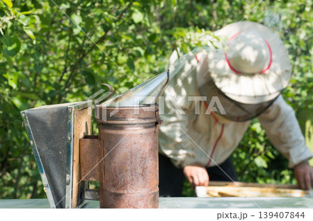 Bee smoker tool against the beekeeper with beehives 139407844