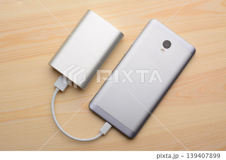 Silver smartphone charging with a power bank on a light wooden background 139407899