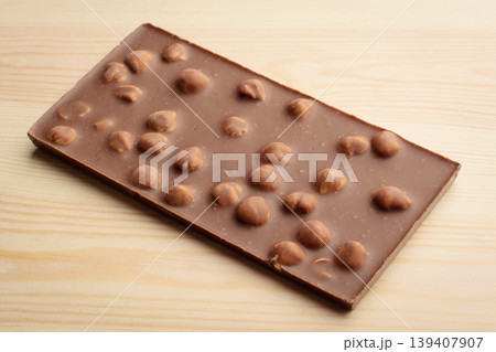 Bar of milk chocolate with nuts on light wooden background 139407907