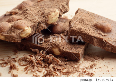 Broken bar of chocolate with nuts seasoned with cocoa powder and grind chocolate lays on wooden table Broken bar of chocolate with nuts seasoned with cocoa powder and grind chocolate lays on wooden table 139407913