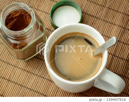 Photo of coffee in a white cup and spoon standing near the jar of coffee and green cover. Making aromatic coffee 139407918