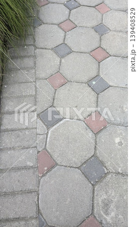 Vertical view displays octagonal pavement tiles with red, dark grey diamond accents. Green plants border the textured concrete walkway. Ideal for urban landscaping, garden design, outdoor projects. Vertical view displays octagonal pavement tiles with red, dark grey diamond accents. Green plants border the textured concrete walkway. Ideal for urban landscaping, garden design, outdoor projects. 139408529