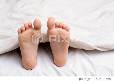Pair of little girl`s feet in a bed. Small girl sleeps in a bed and her bare feet are visible from under the blanket 139408660