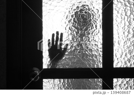 The silhouette of the person and its hand behind the door with the textured glass 139408687