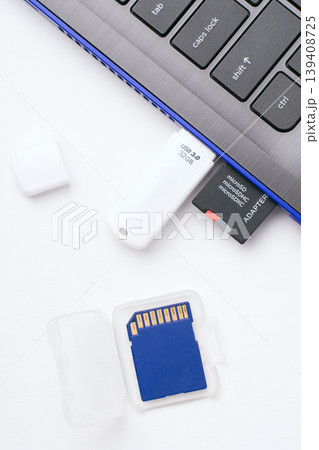 MicroSD memory card with adapter, white USB stick plugged in the ports of the modern blue laptop. One more blue SD memory card in a transparent case lays near the computer. Top view. 139408725