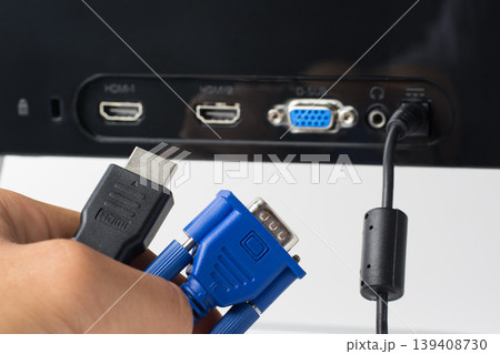 Man`s hand holds HDMI and VGA cables against a monitor with ports. Choise between modern HDMI and old VGA connection Man`s hand holds HDMI and VGA cables against a monitor with ports. Choise between modern HDMI and old VGA connection 139408730
