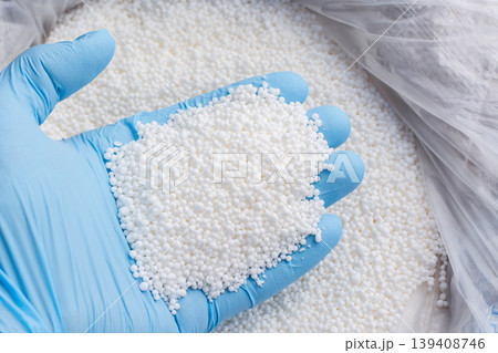 Closeup photo of a hand in blue glove holds white fertilizer for plants. Big bag with chemical NPK fertilizer for plants 139408746