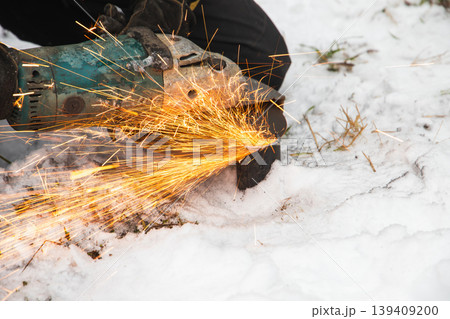 Worker uses an angle grinder to cut metal outdoors, producing bright orange sparks Worker uses an angle grinder to cut metal outdoors, producing bright orange sparks 139409200