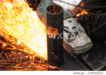 Worker using an angle grinder to cut a steel pipe, sending bright orange sparks Worker using an angle grinder to cut a steel pipe, sending bright orange sparks 139409201