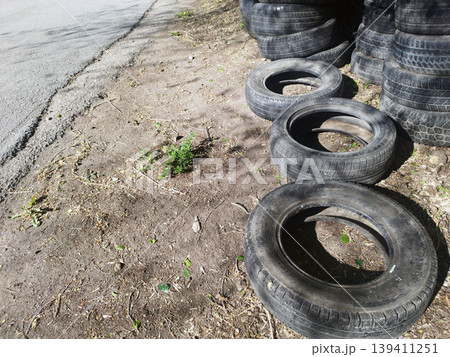: Stack of discarded black car tires piled along a dirt roadside. The image captures environmental waste and industrial materials left outdoors, highlighting themes of recycling and pollution 139411251