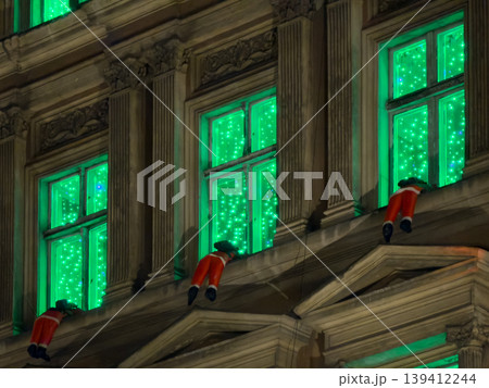 A historic building facade showcases vibrant green sparkling lights and whimsical red elf figures, creating a charming festive urban Christmas holiday decoration A historic building facade showcases vibrant green sparkling lights and whimsical red elf figures, creating a charming festive urban Christmas holiday decoration 139412244
