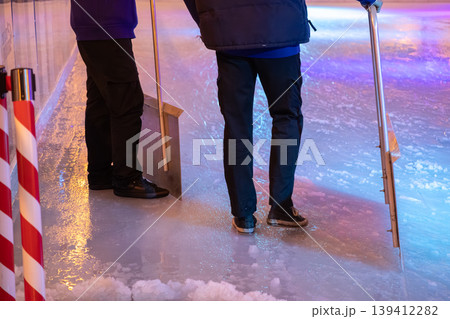 Ice rink workers clearing glossy surface with specialized tools under vibrant colorful lights, preparing for public winter skating fun and recreation 139412282