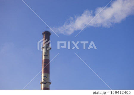 Tall industrial chimney emitting thick white smoke against a clear blue sky, symbolizing industrial activity, energy production, and environmental pollution Tall industrial chimney emitting thick white smoke against a clear blue sky, symbolizing industrial activity, energy production, and environmental pollution 139412400