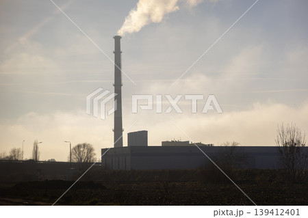 Tall industrial chimney emitting thick white smoke into a hazy winter sky, showcasing factory operations and environmental impact Tall industrial chimney emitting thick white smoke into a hazy winter sky, showcasing factory operations and environmental impact 139412401