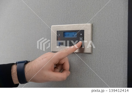 Hand adjusting smart digital thermostat display for climate control in modern office or hotel, emphasizing energy efficiency and personalized comfort Hand adjusting smart digital thermostat display for climate control in modern office or hotel, emphasizing energy efficiency and personalized comfort 139412414