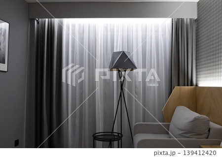 Contemporary interior design showcases a modern geometric floor lamp and sheer curtains, creating a tranquil and stylish atmosphere for home comfort and relaxation 139412420