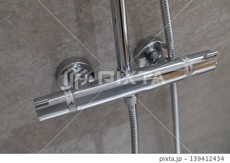 Modern chrome thermostatic shower mixer tap mounted on a grey tiled wall, featuring temperature controls and 40 marking for precise water regulation in a contemporary bathroom 139412434