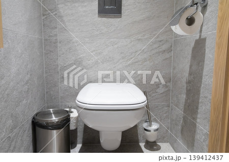 A modern toilet in a grey tiled bathroom features a sleek design, essential hygiene accessories, and functional elements for contemporary spaces A modern toilet in a grey tiled bathroom features a sleek design, essential hygiene accessories, and functional elements for contemporary spaces 139412437