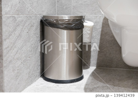Sleek stainless steel waste bin with a black liner, positioned in a modern tiled public restroom to maintain excellent hygiene and cleanliness standards Sleek stainless steel waste bin with a black liner, positioned in a modern tiled public restroom to maintain excellent hygiene and cleanliness standards 139412439