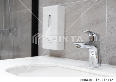 Modern bathroom featuring a gleaming chrome faucet and a white wall-mounted tissue dispenser, emphasizing cleanliness and contemporary design Modern bathroom featuring a gleaming chrome faucet and a white wall-mounted tissue dispenser, emphasizing cleanliness and contemporary design 139412442