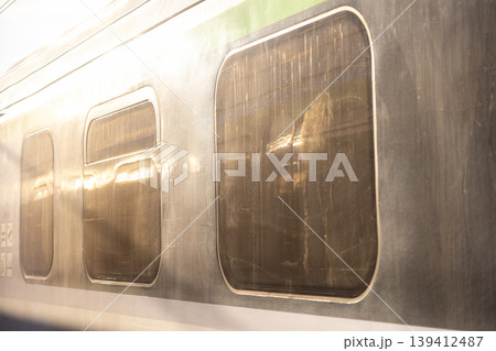 Modern train's metallic side features dirty, reflective windows, mirroring urban light and symbolizing efficient public transportation travel Modern train's metallic side features dirty, reflective windows, mirroring urban light and symbolizing efficient public transportation travel 139412487