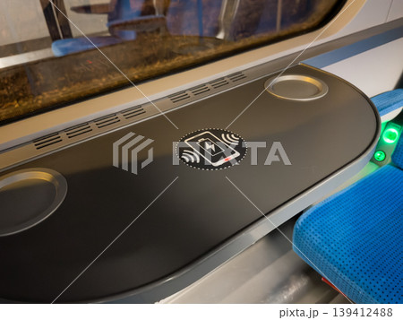 Modern high-speed train tray table offering integrated wireless phone charging symbol, ensuring convenient mobile device power and an enhanced passenger travel experience Modern high-speed train tray table offering integrated wireless phone charging symbol, ensuring convenient mobile device power and an enhanced passenger travel experience 139412488