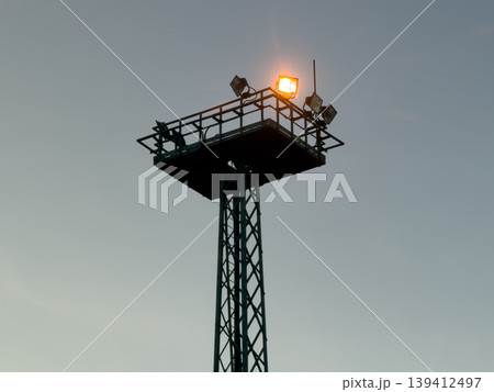 Lattice metal tower with bright floodlight glowing on its platform, providing robust security lighting and crucial nighttime surveillance for industrial infrastructure 139412497