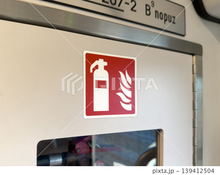Red fire extinguisher sign with flame icon on a white wall, highlighting crucial emergency safety procedures and equipment availability in public transit Red fire extinguisher sign with flame icon on a white wall, highlighting crucial emergency safety procedures and equipment availability in public transit 139412504