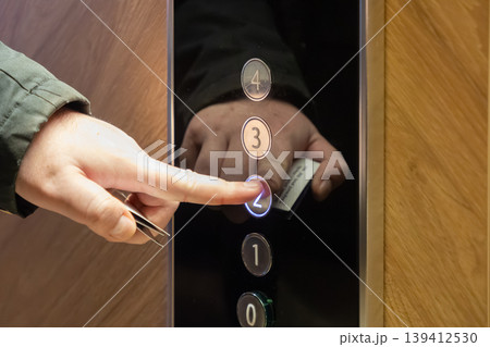Human hand presses brightly illuminated elevator button for floor two, holding a key card for secure access and modern building navigation Human hand presses brightly illuminated elevator button for floor two, holding a key card for secure access and modern building navigation 139412530