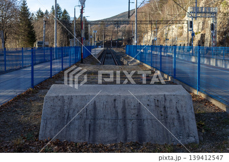 A remote railway track extends through a natural mountain landscape, protected by vibrant blue fences, symbolizing travel, connection, and robust transportation infrastructure 139412547