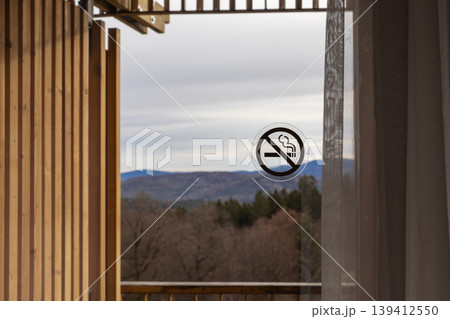 No smoking prohibition sign clearly displayed on a hotel balcony's glass door, overlooking a picturesque autumn mountain landscape, promoting health and safety No smoking prohibition sign clearly displayed on a hotel balcony's glass door, overlooking a picturesque autumn mountain landscape, promoting health and safety 139412550