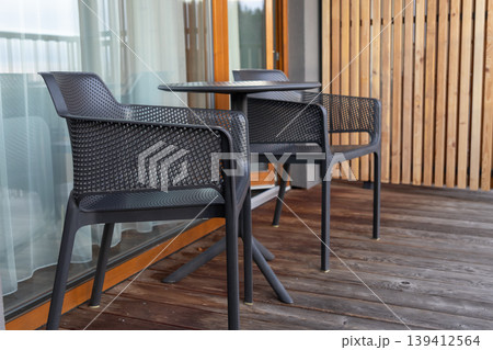 Two modern black chairs with a matching round table are set on a wooden balcony deck, providing a comfortable outdoor seating area for relaxation and leisure Two modern black chairs with a matching round table are set on a wooden balcony deck, providing a comfortable outdoor seating area for relaxation and leisure 139412564