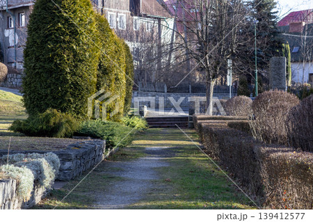 Peaceful garden path winding through lush evergreen trees and dormant hedges towards stone stairs, capturing suburban tranquility and natural outdoor landscaping Peaceful garden path winding through lush evergreen trees and dormant hedges towards stone stairs, capturing suburban tranquility and natural outdoor landscaping 139412577