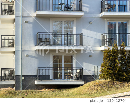 Modern apartment building facade with multiple balconies featuring outdoor furniture, showcasing clean contemporary design for urban residential living Modern apartment building facade with multiple balconies featuring outdoor furniture, showcasing clean contemporary design for urban residential living 139412704