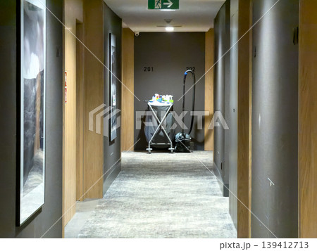 Modern hotel corridor features a housekeeping cart and vacuum, signifying routine service and pristine maintenance for an optimal guest experience Modern hotel corridor features a housekeeping cart and vacuum, signifying routine service and pristine maintenance for an optimal guest experience 139412713
