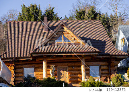 Rustic wooden log cabin house with a brown tiled roof and triangular window, surrounded by green trees, offering a peaceful and natural living environment 139412873